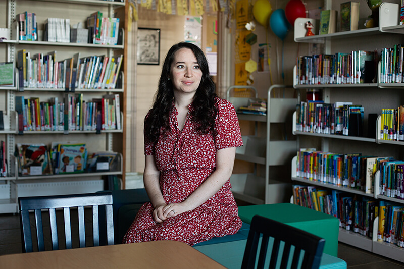 Lady sitting in a red dress between bookshelves.