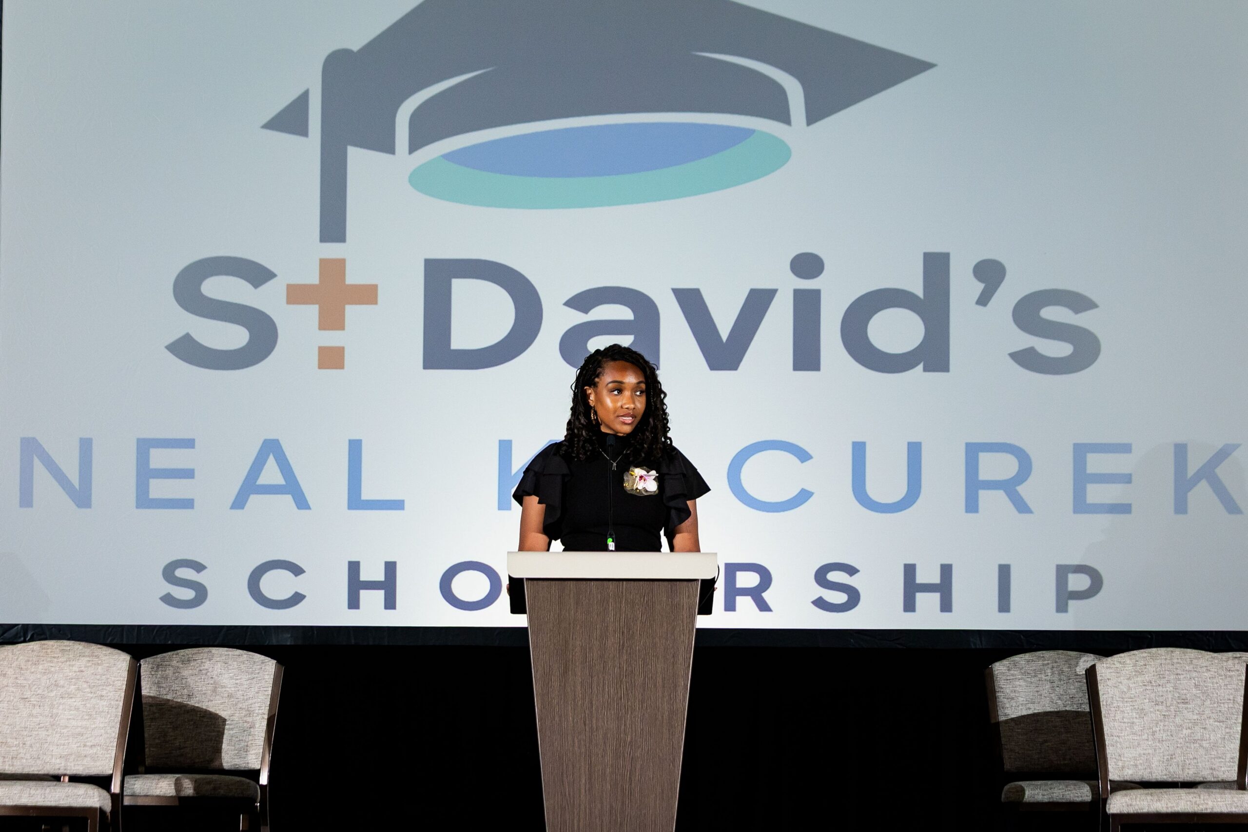 A scholar speaks at a podium in front of a St David's foundation slideshow